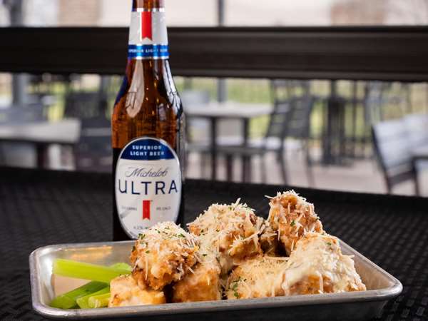 A tray of chicken wings on an outdoor patio table next to a bottle of Michelob Ultra.